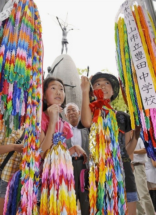 duas crianças japonesas segurando cordoes coloridos de tsuru origami